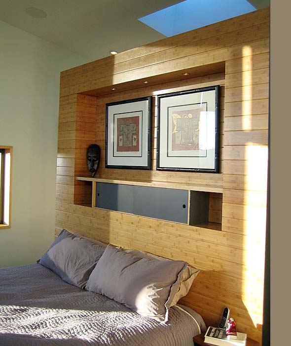 Bedroom with a wooden recessed wall unit featuring framed artwork, a decorative mask, and natural light from a skylight.