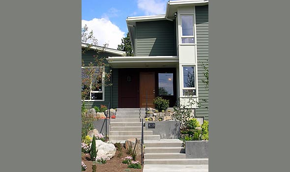 Entrance of a green two-story house with concrete steps and landscaping including rocks and plants.
