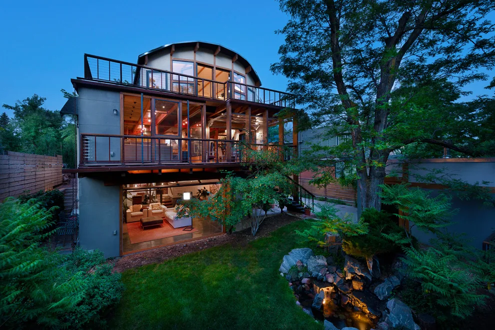 Rear exterior view of a modern multi-level home with large glass walls and a curved roof at twilight.