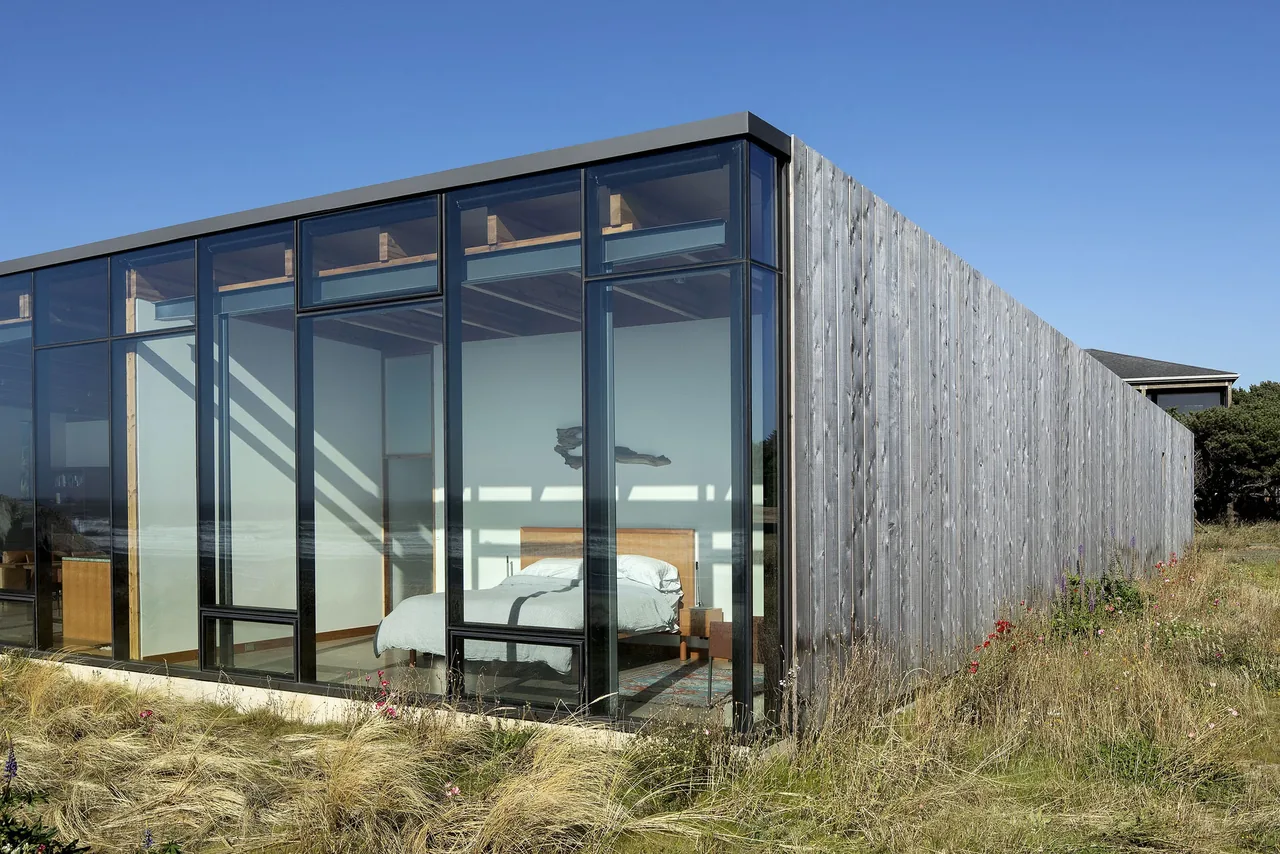 Exterior view of a modern beach house with one side clad in vertical wooden planks and the other side featuring large floor-to-ceiling glass