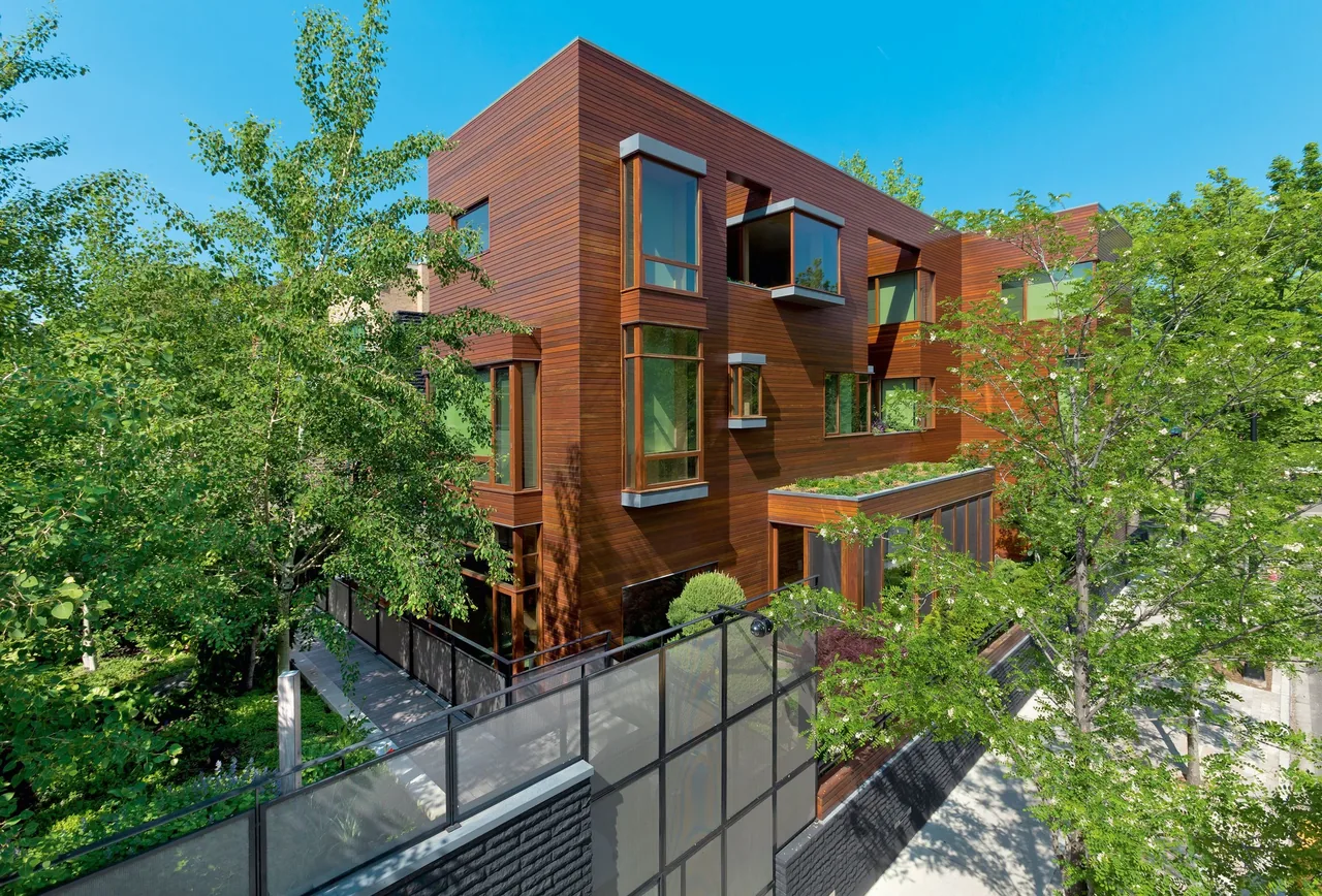 Modern three-story residence clad in horizontal wooden panels with multiple corner and large windows, surrounded by trees and greenery.