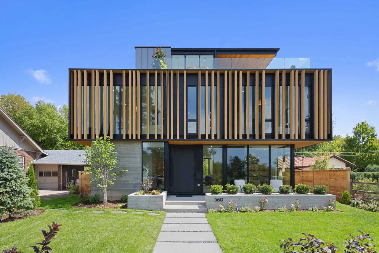 Front exterior of a modern two-story house with vertical wooden slats on the upper level and a concrete base, featuring large windows and a