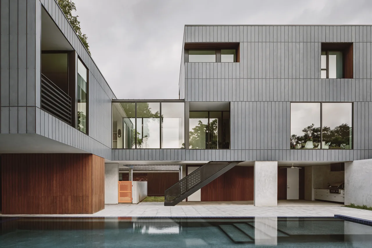 Modern home exterior with gray vertical paneling, large windows, wooden accent walls, and a pool in the foreground.