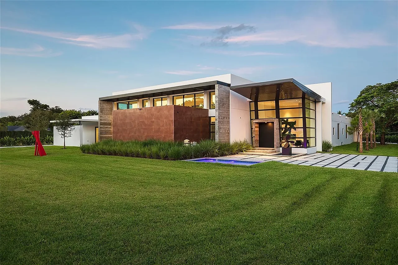 Modern single-story house with large front glass windows and a landscaped lawn at sunset.