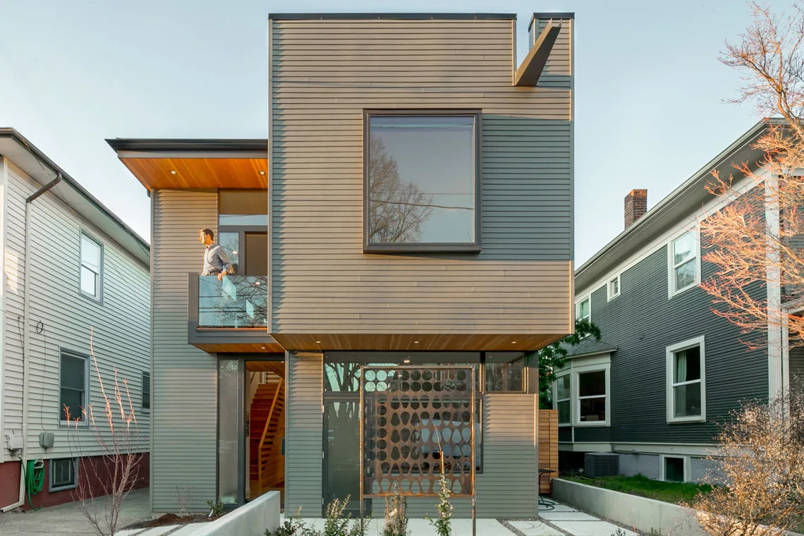 Front exterior of a modern two-story house with wood siding and a glass balcony.