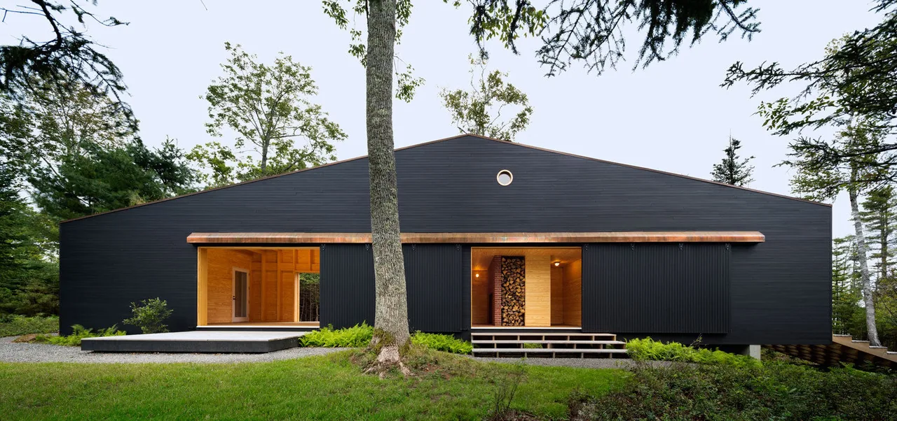Black boathouse with sliding doors open to wood interior and a small porthole window above.