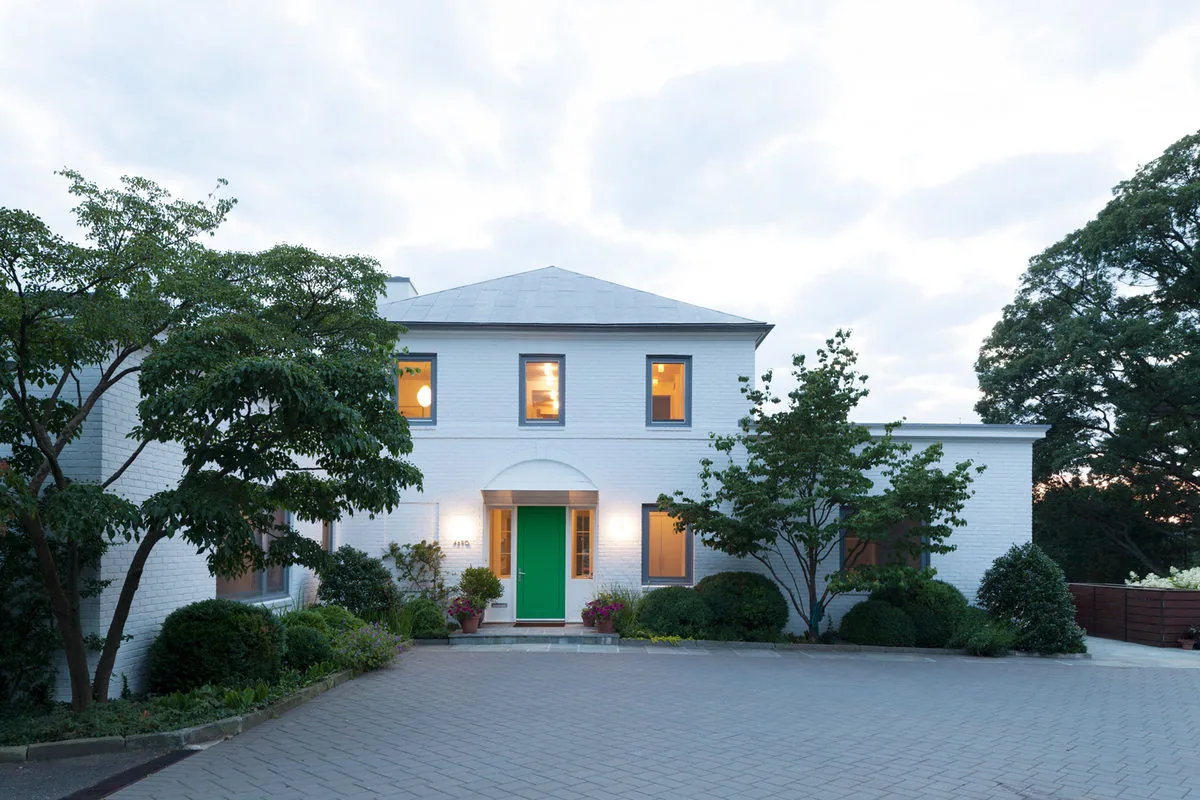 Front view of a white brick two-story house with a green door and symmetrical windows at dusk.
