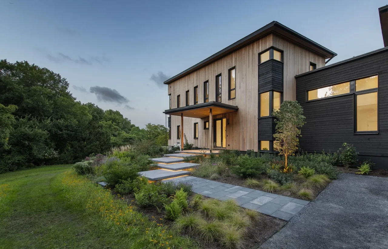 Exterior view of a modern two-story house with vertical wood siding and large windows during dusk.