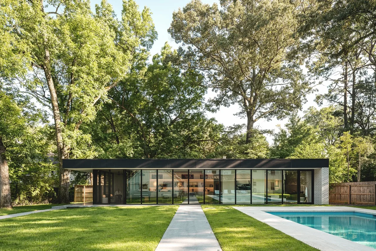 Single-story modern house with large floor-to-ceiling windows facing a backyard with a pool and lawn.