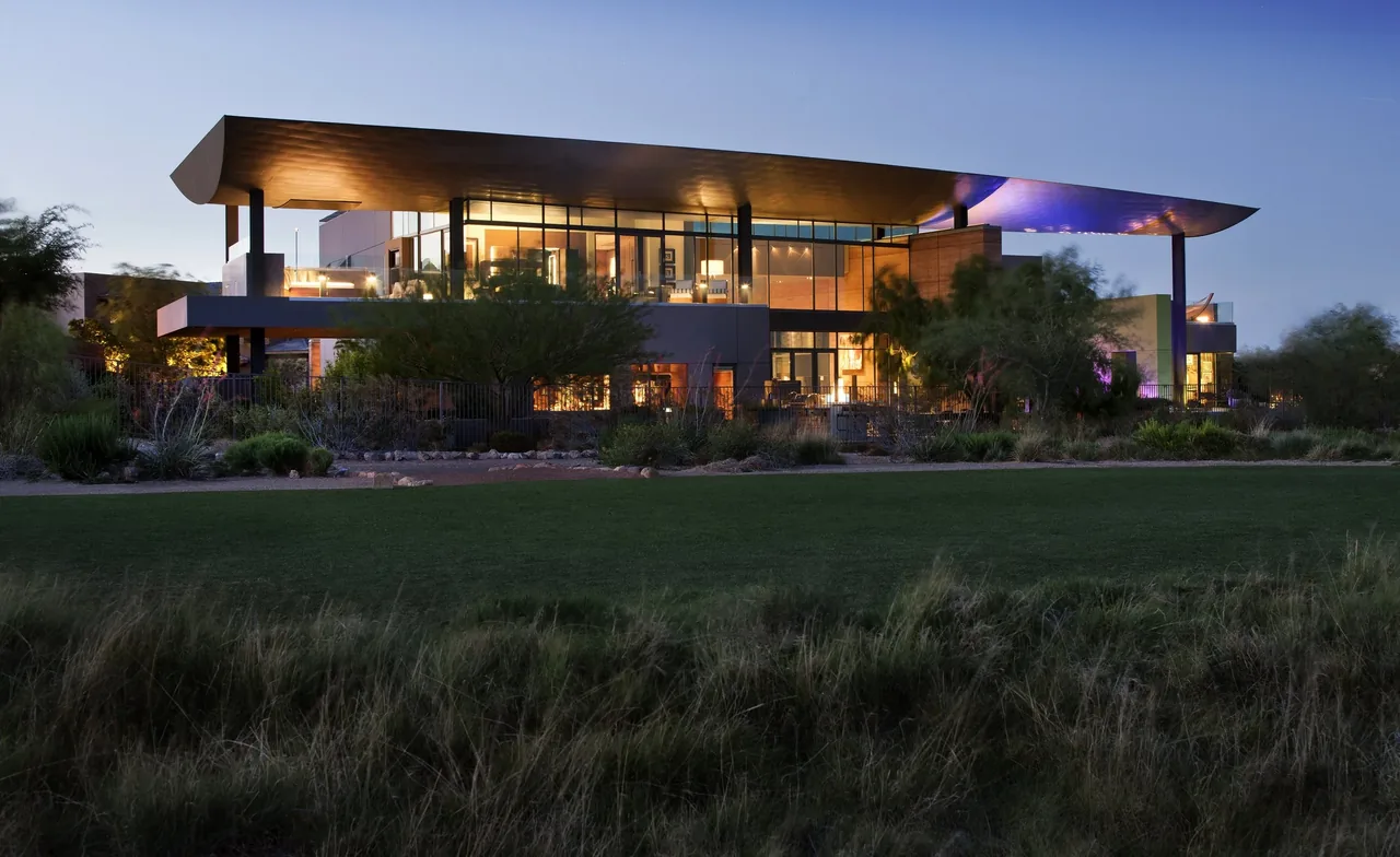 Modern house exterior at dusk with large overhanging roof and extensive glass walls.