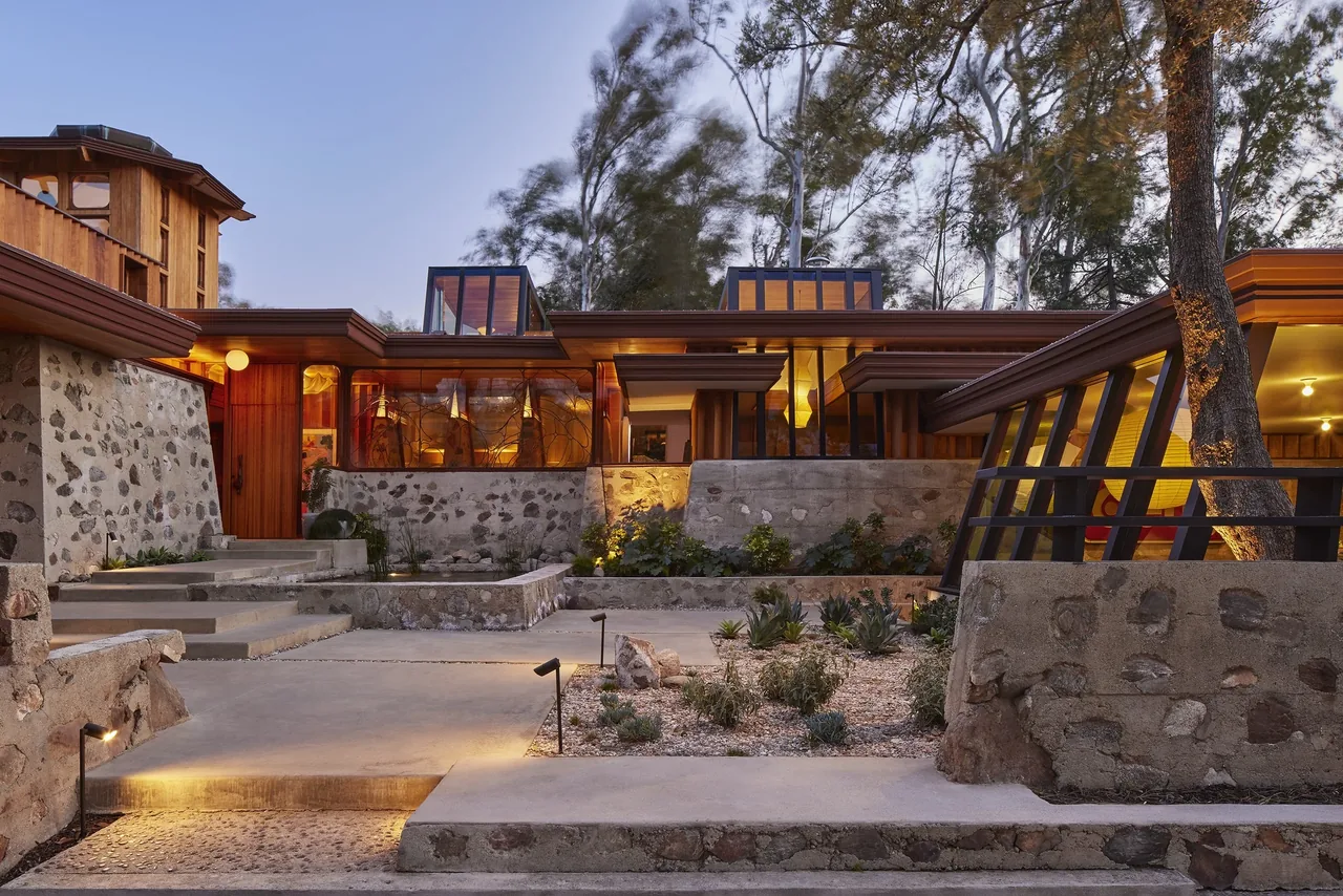 View of a residence exterior at dusk showing stone walls, large windows, and landscaped yard with outdoor lighting.