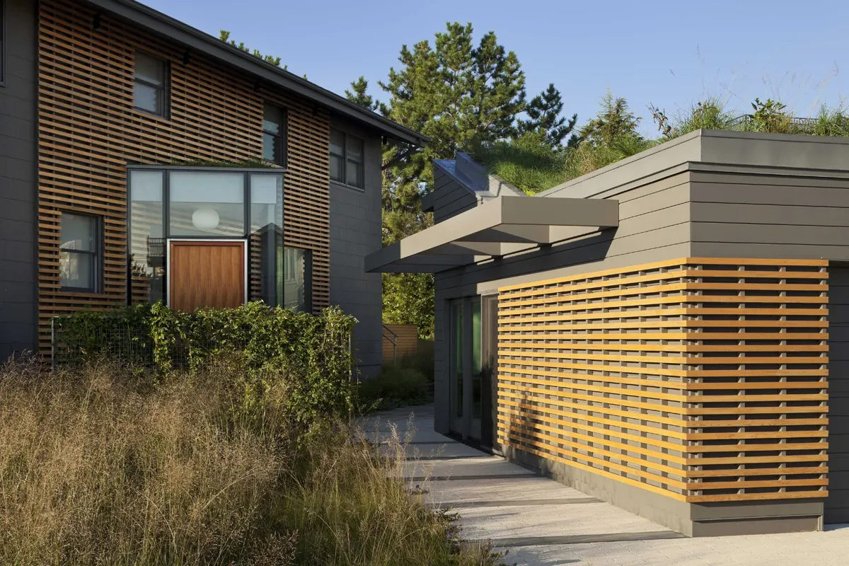 Two modern buildings with gray siding, one with a green roof and the other with wood slat accents on facade.