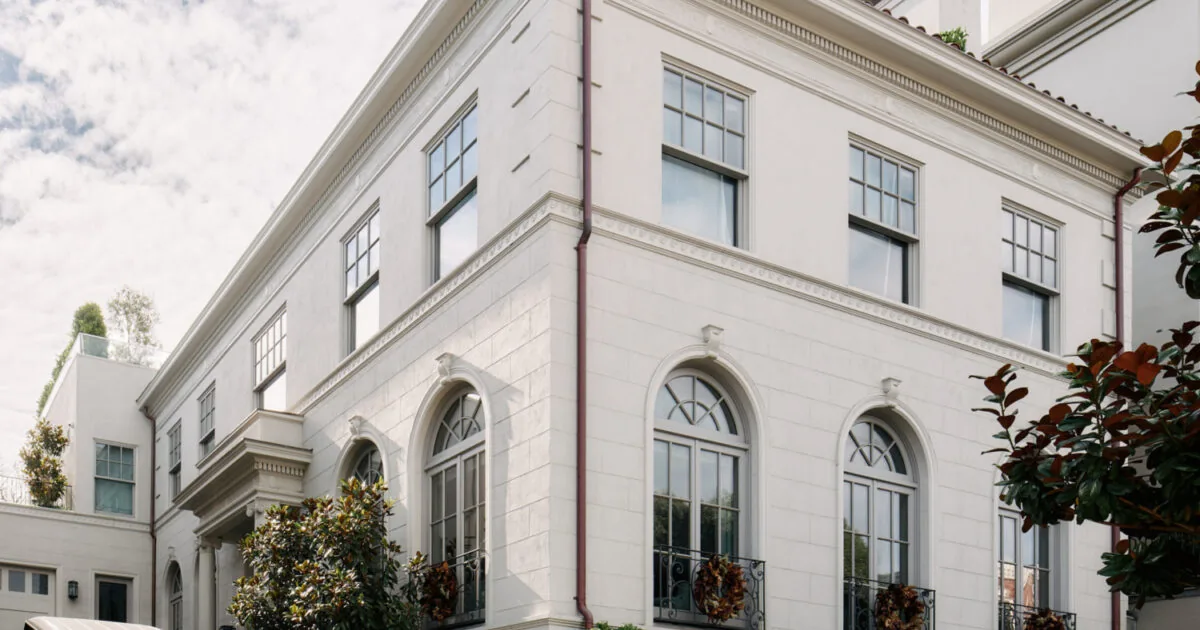 Exterior corner view of a large two-story traditional white stucco house with arched windows and decorative wreaths.