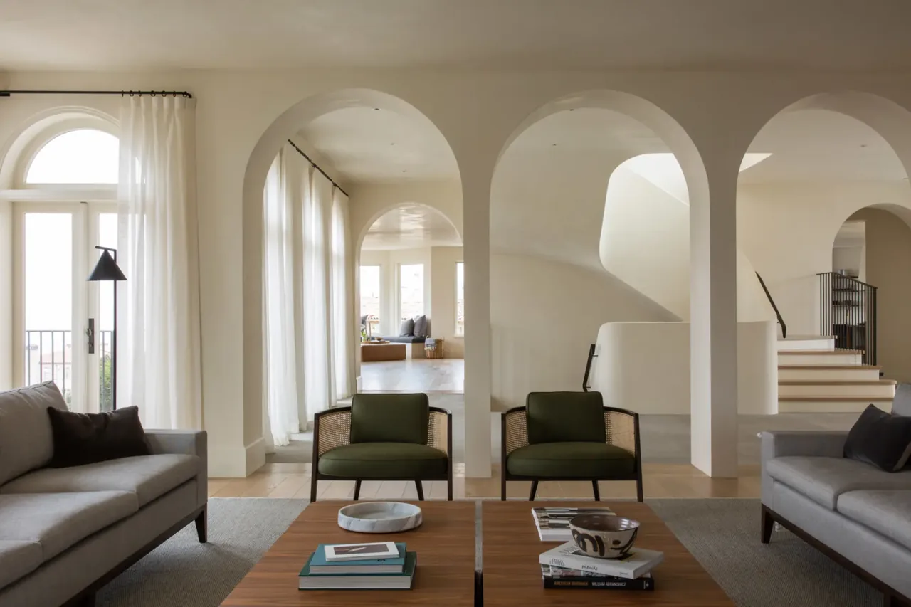 Living room with neutral colors, arched openings, two green chairs, and two gray sofas facing a wooden coffee table.