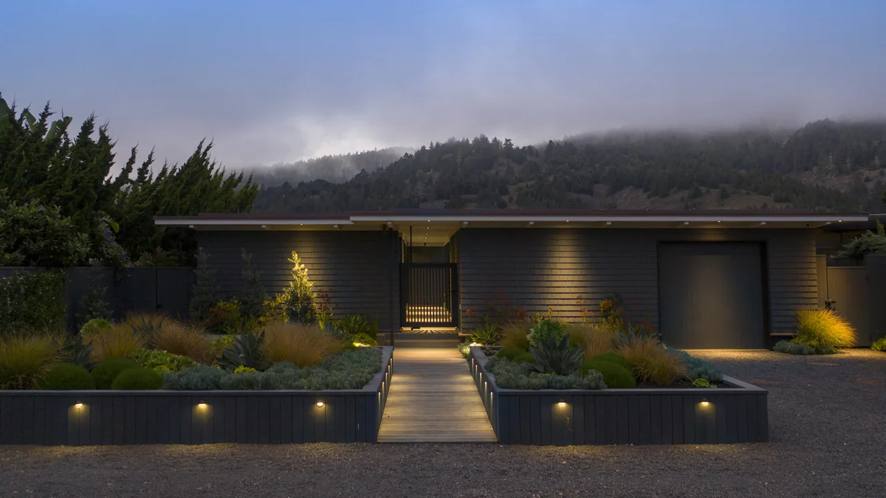 Single-story modern bungalow at dusk with lit pathway and manicured landscaping.