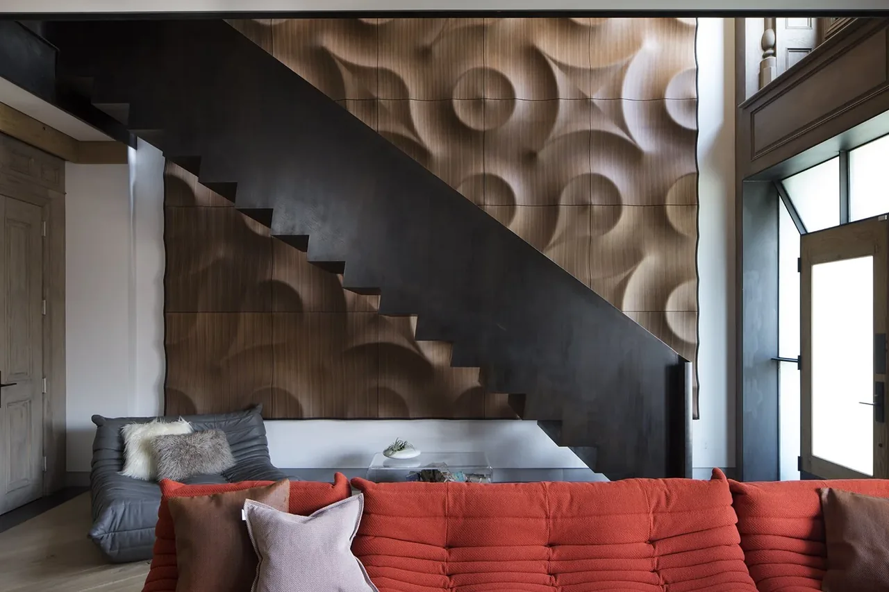 Interior view of a living room with a black metal floating staircase and a textured wooden wall panel behind it.