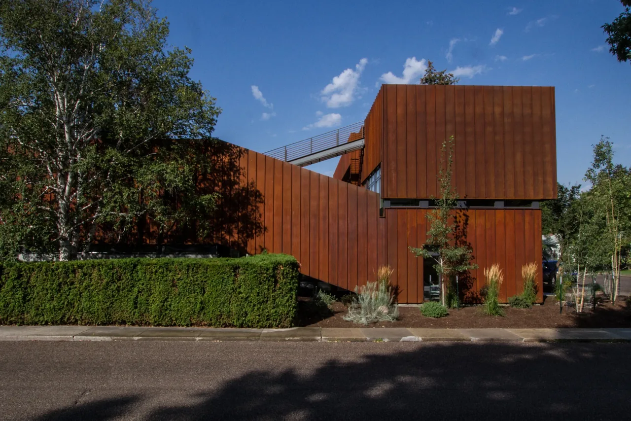 Exterior view of a residential building with rust-colored metal siding and angled design under a clear blue sky.