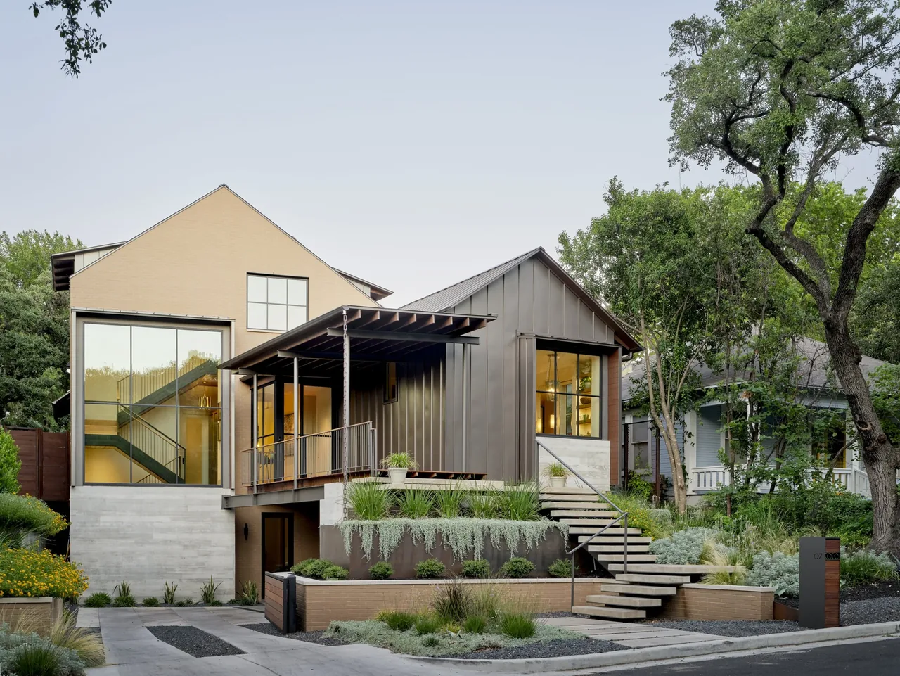 Exterior view of a modern hillside residence with a staircase leading to a covered porch and large windows.