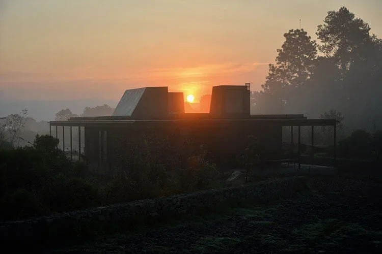 Silhouetted modern house with flat roof and large windows at sunrise in a misty landscape.