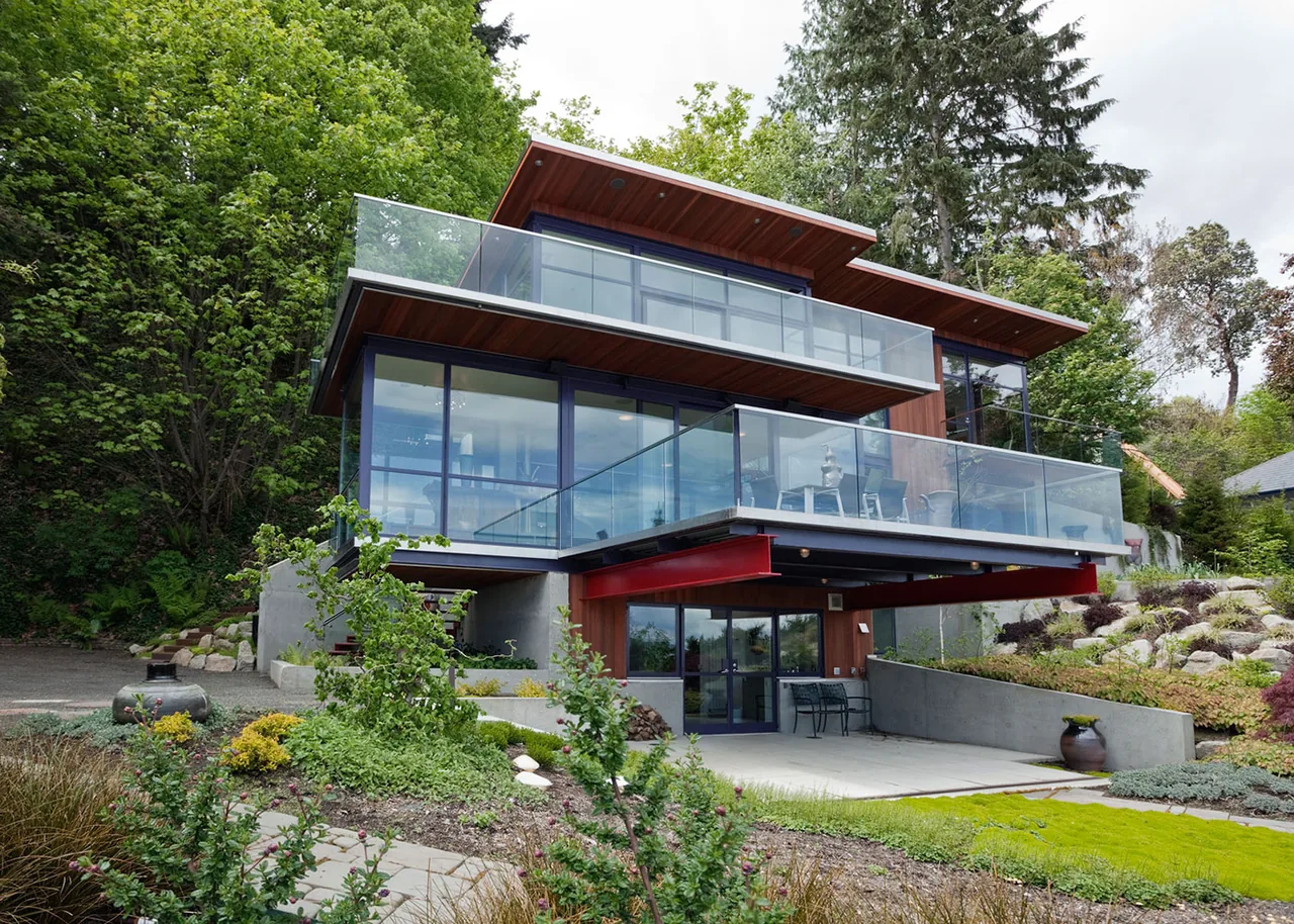 Modern multi-story guest residence with extensive glass balconies and wood soffits set on a landscaped hillside.