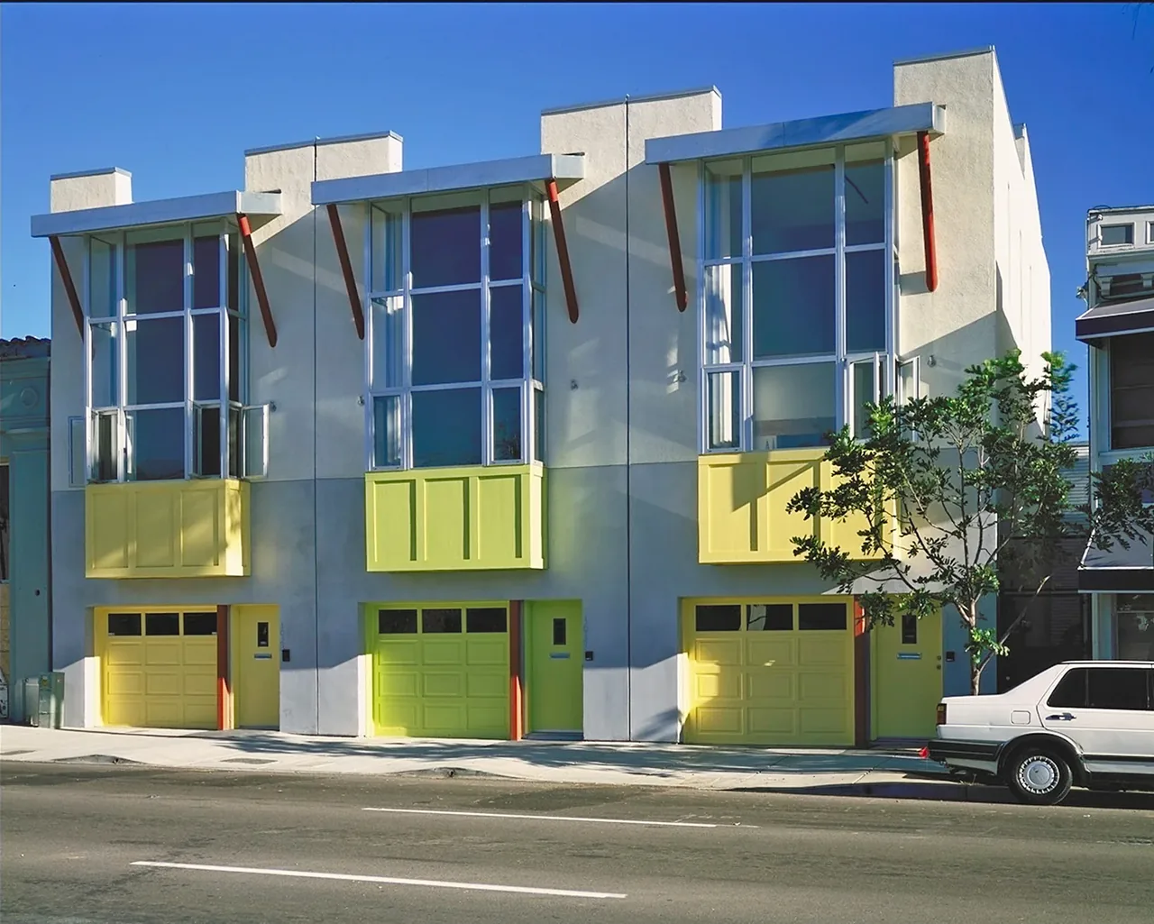 Contemporary three-unit residential building with large glass windows and bright yellow garage doors and balconies.