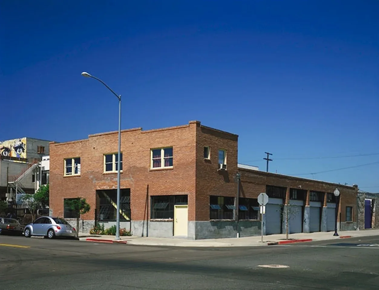Two-story brick building with multiple large windows and garage doors on a corner lot under a clear blue sky.