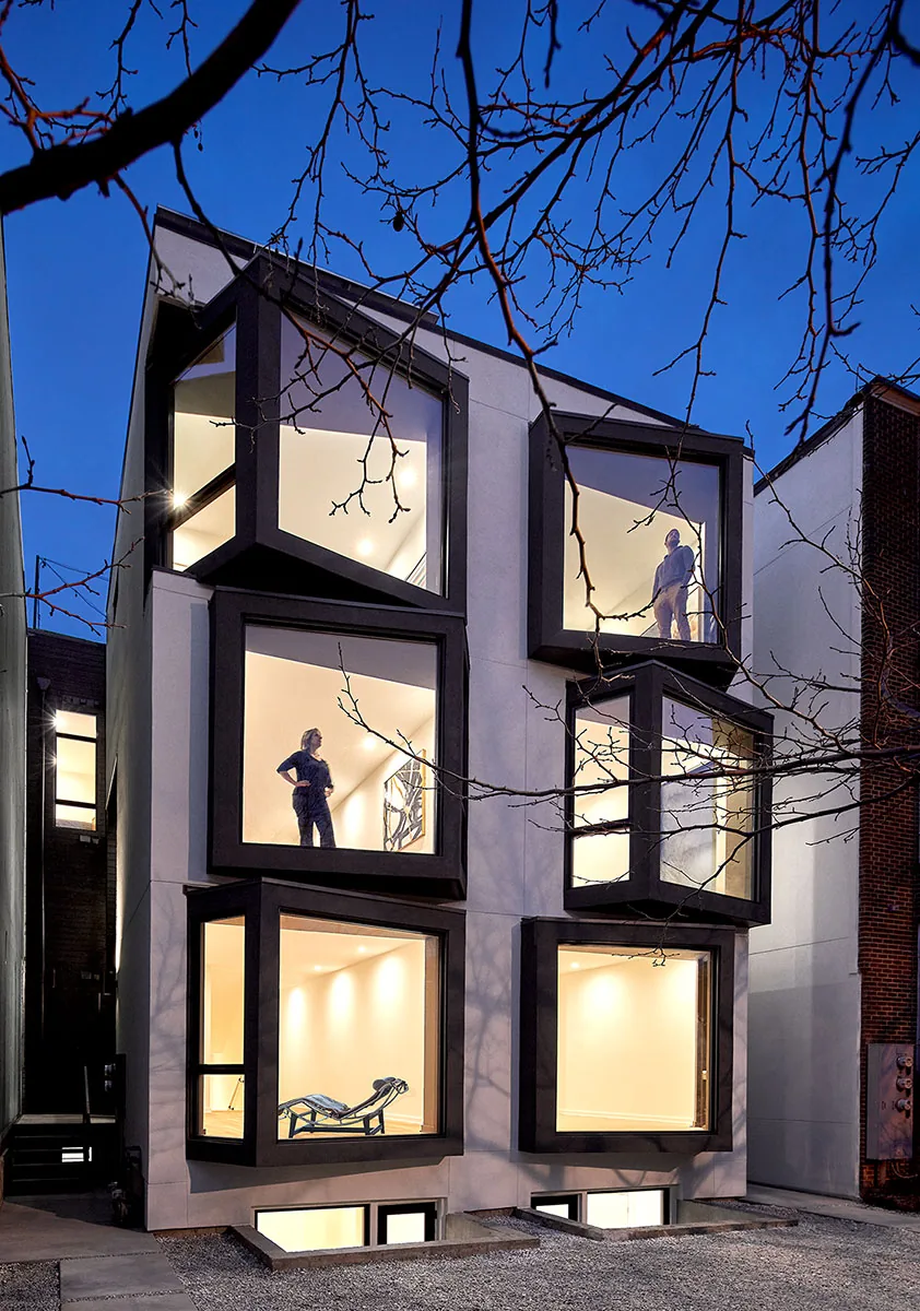 Modern multi-story house at dusk with large cube-shaped windows and minimal exterior detail.