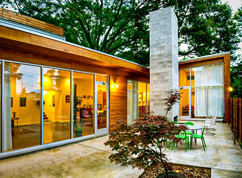 Outdoor courtyard area of a modern home with large glass doors, wood siding, and a tall concrete fireplace.