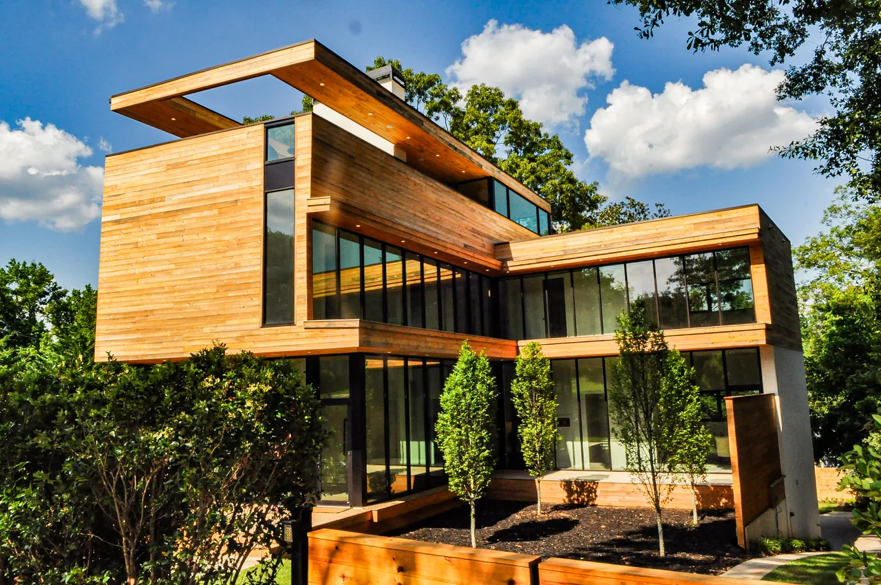 Modern two-story house with natural wood siding and large black-framed windows under a blue sky.