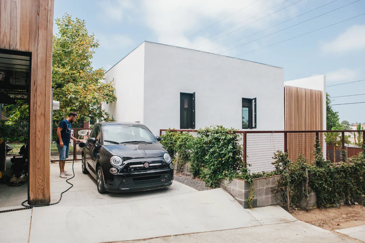 A modern white stucco house with flat roof viewed from the driveway with a man charging a black car.