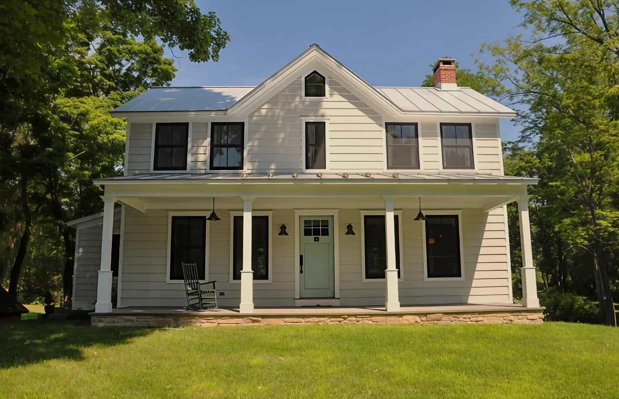 Front view of a two-story white farmhouse with a covered porch and metal roof under blue sky.