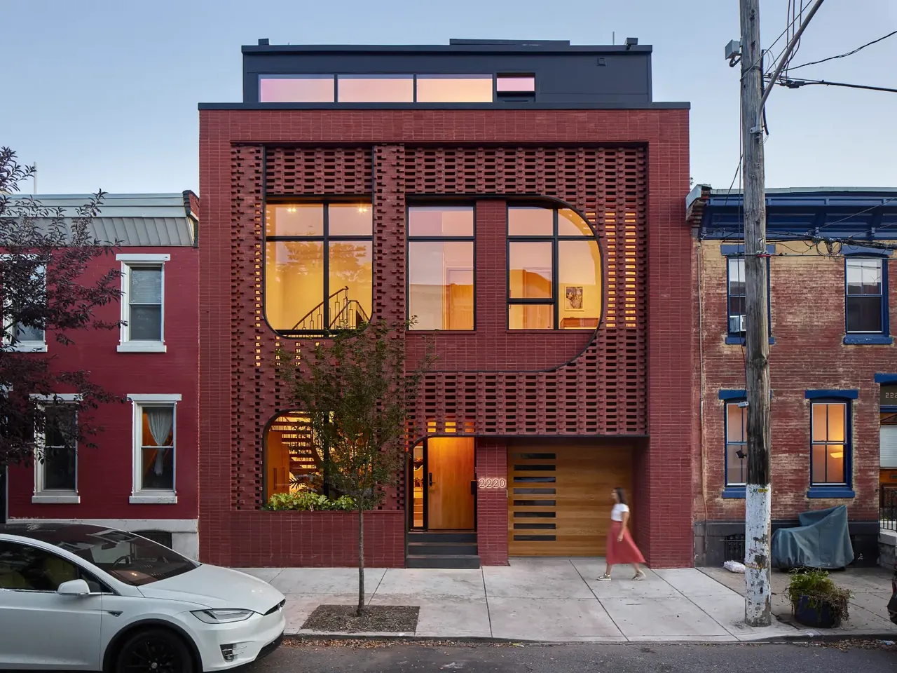 Exterior front view of a modern brick house with a patterned brick facade and large windows at dusk.