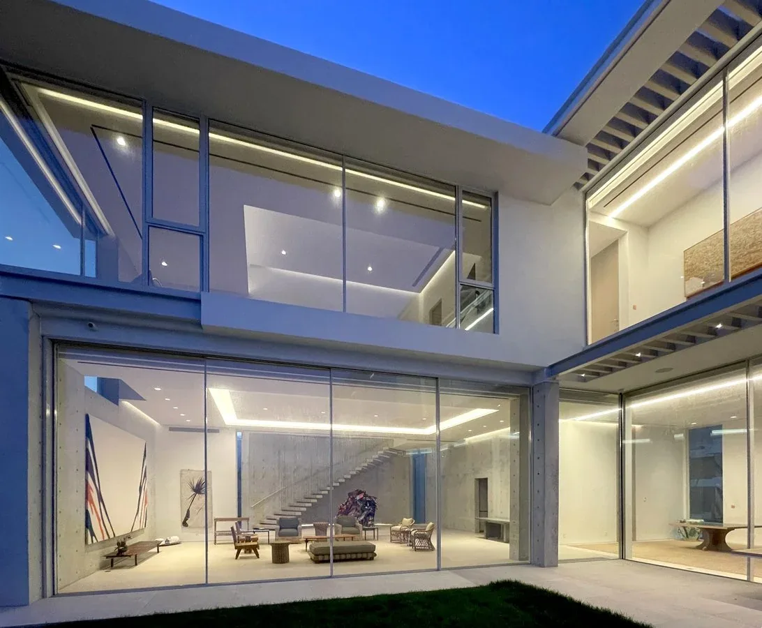 Exterior view of a modern two-story house at dusk with large floor-to-ceiling glass windows revealing an open living area inside.