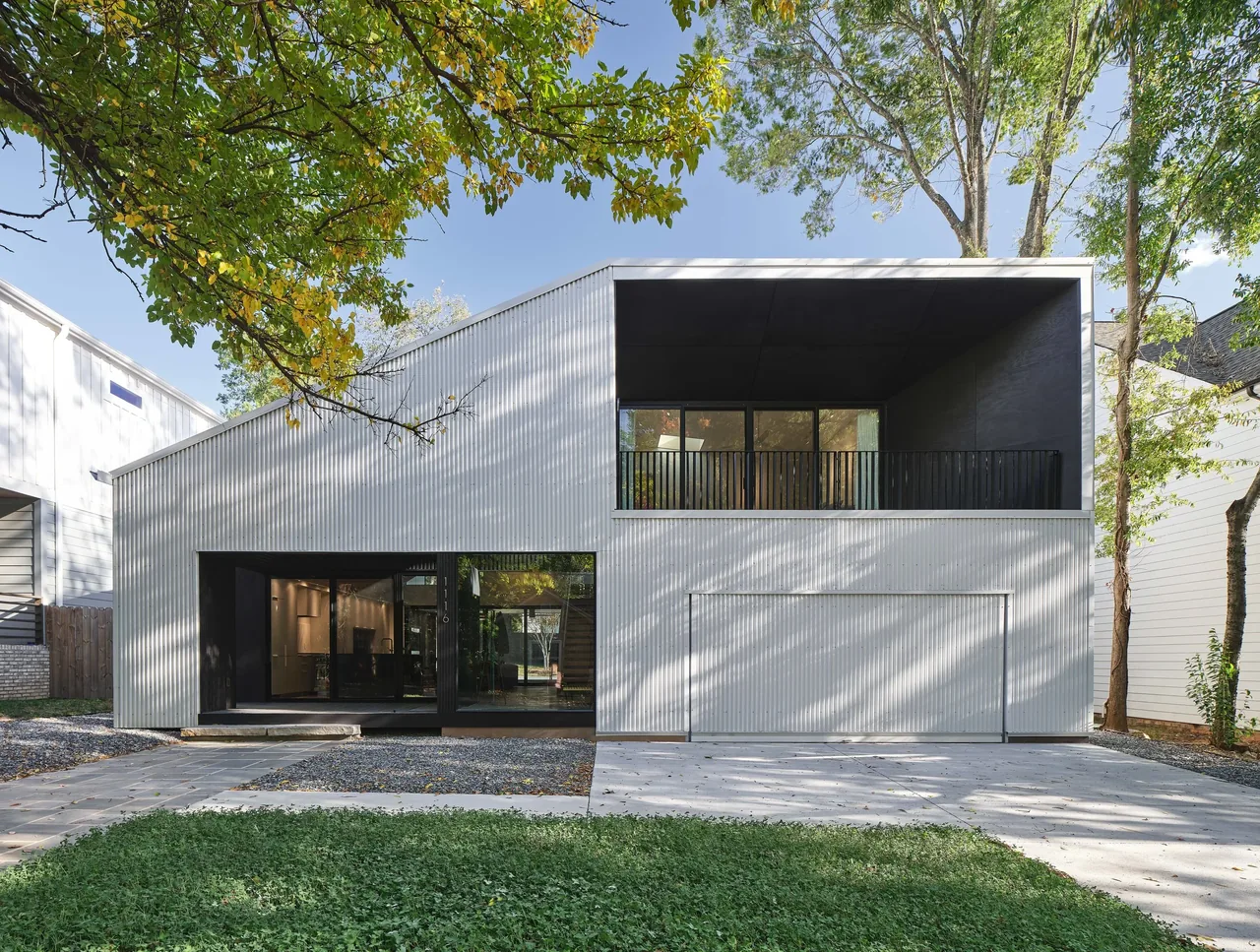 Modern two-story house with corrugated metal siding, large black-framed windows, and a recessed second-story balcony.