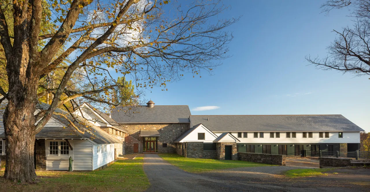 Exterior view of a large barn-style building with stone and white siding under a clear blue sky.