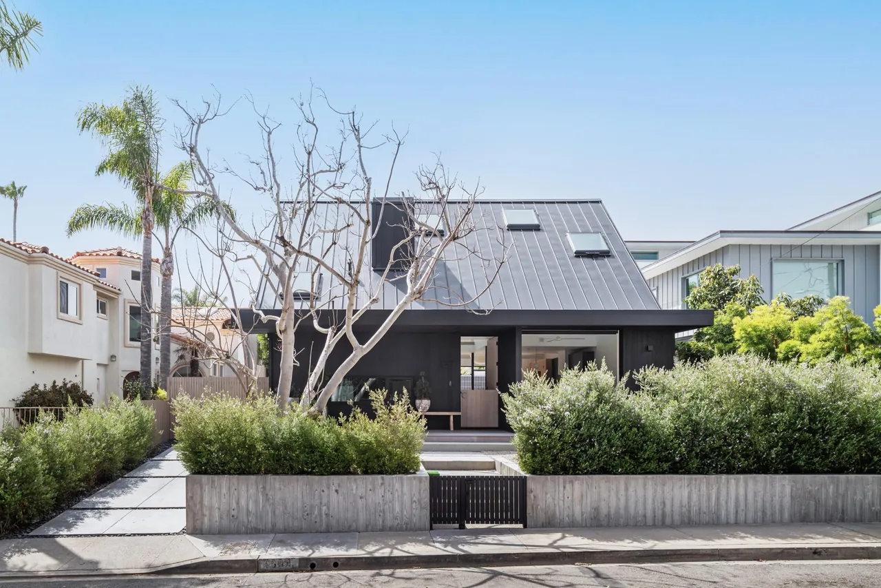 Front exterior view of a modern house with a steep standing seam metal roof and hidden entrance behind greenery.
