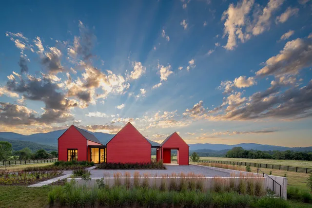 A red farmhouse with gable roofs set in a rural landscape under a partly cloudy sky at sunset.