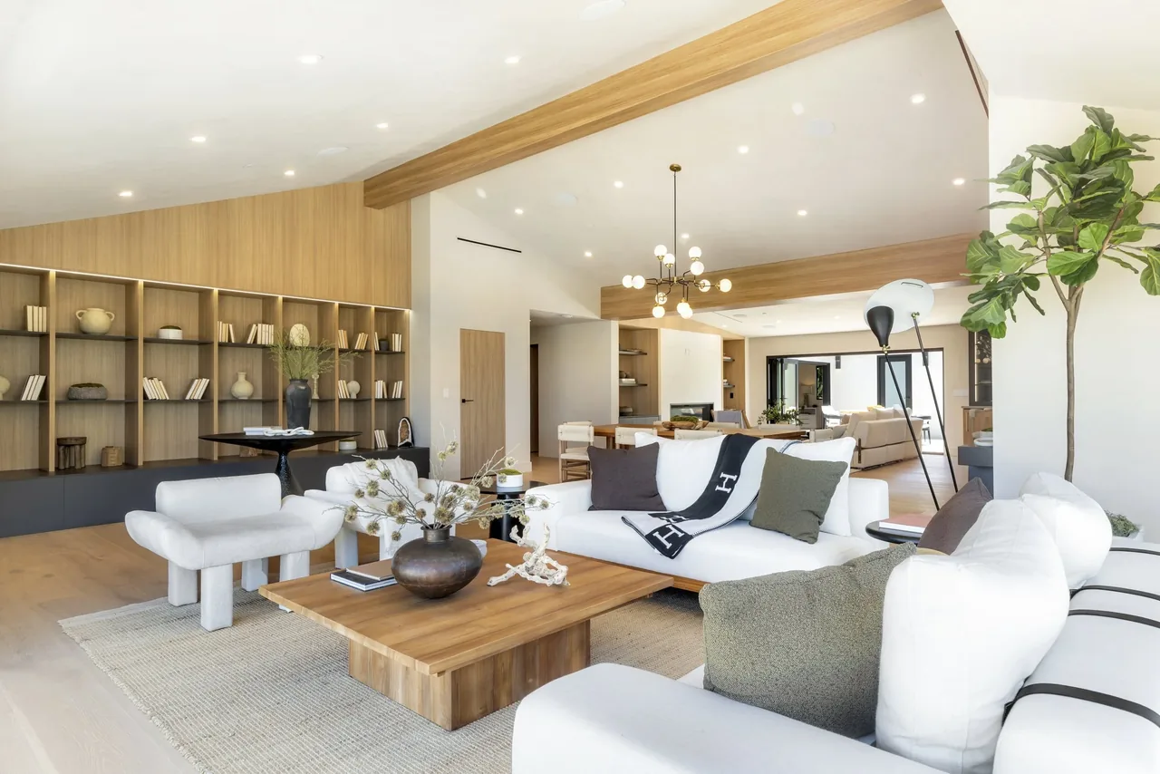 Bright modern living room with white sofas, wood coffee table, and built-in wood bookshelf wall.