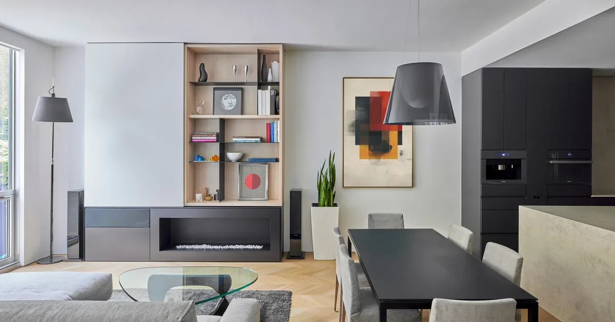 Modern open living and dining area with glass coffee table, built-in shelving, and black kitchen cabinetry.