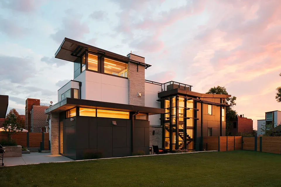 Modern multi-story home exterior at sunset with large windows and mixed materials.