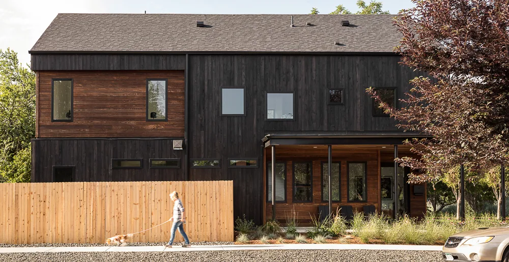 Modern two-story house with dark wood siding and a front porch under a gable roof.