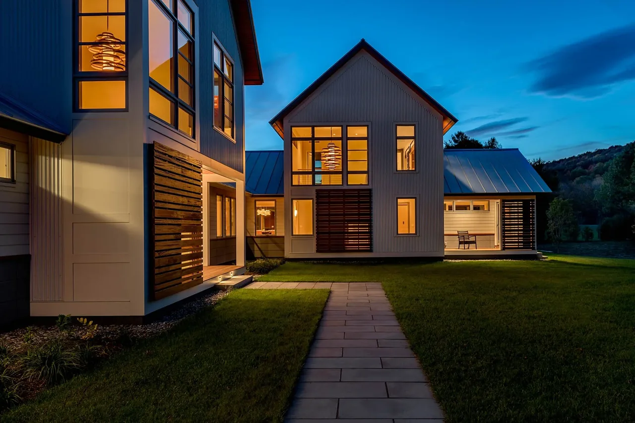 Evening view of a modern two-story house with multiple large windows and wooden slat accents.