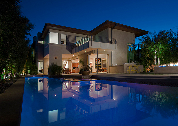 Night view of a two-story modern house with open rear patio and pool reflecting the building and evening sky.
