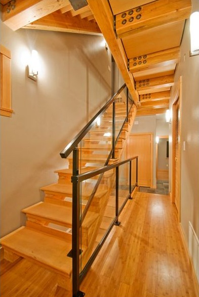 Wooden staircase with glass and black metal railing in a hallway with exposed wood ceiling beams.