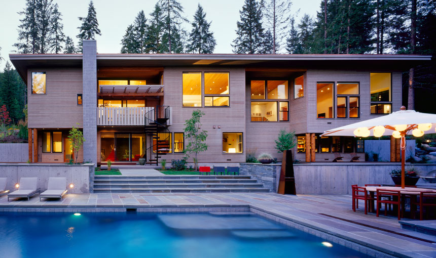 Modern two-story house with extensive glazing and an outdoor pool area surrounded by greenery.