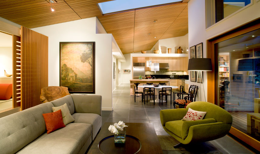 Modern living room and kitchen with wood ceiling, tiled floor, and large sliding glass door to an adjacent room.