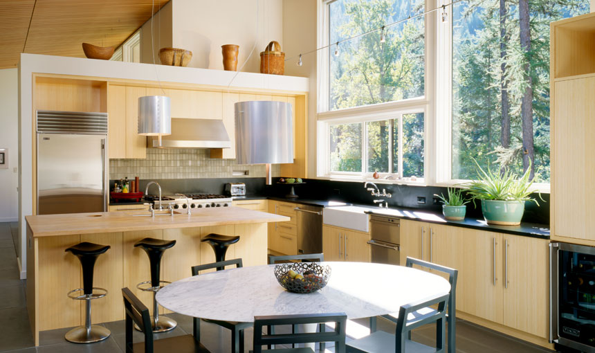 Kitchen featuring wood cabinetry, large windows overlooking trees, and a central island with bar stools.