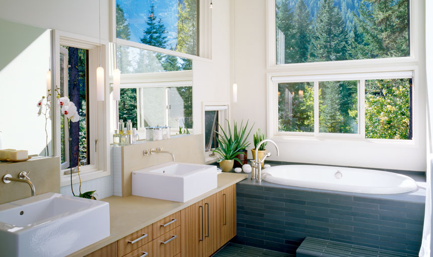 Bright bathroom featuring dual rectangular sinks and a built-in tub with gray tile surround beneath large windows.