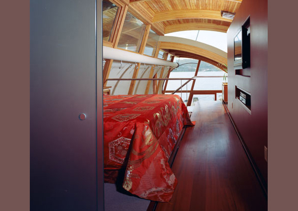 Bedroom interior with curved wooden ceiling and extensive glazing providing panoramic views.