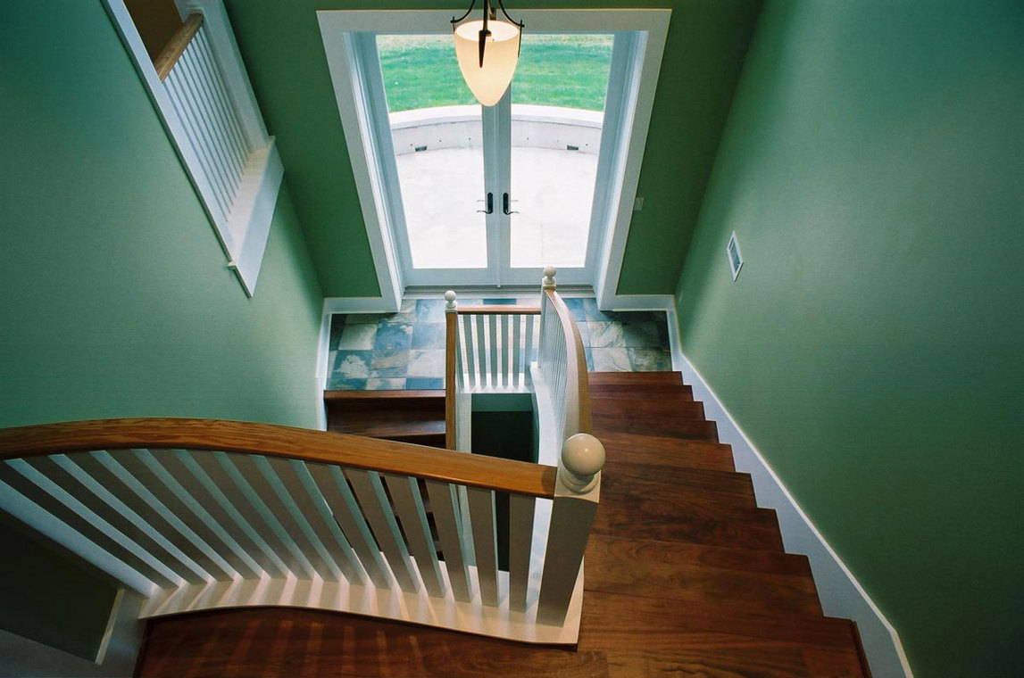 Interior staircase with wood treads and white spindled railings leading to a tiled landing and glass double entry door.